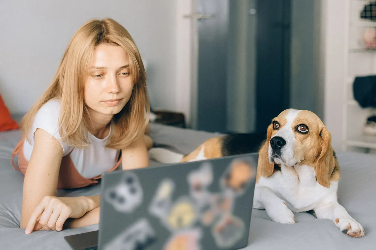 Mujer consultando el portátil en casa con su perro tumbado al lado